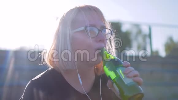 女孩在美丽的阳光下从玻璃瓶里喝水很漂亮的灯光电影慢动作视频的预览图