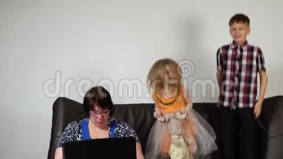 孩子们在沙发上跳跃一个沮丧的祖母正在使用笔记本电脑视频的预览图