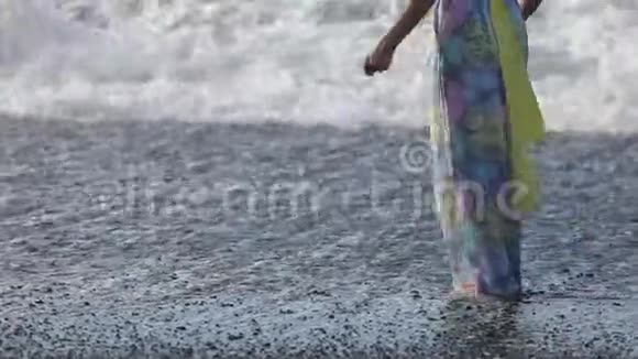 一个穿着连衣裙的年轻女子正在黑色海滩上跳舞和散步波浪向岸边奔流冰岛视频的预览图