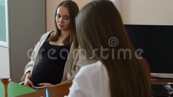 一位年轻的妇产科医生在医院的办公室里带一位怀孕的病人孕妇问视频的预览图