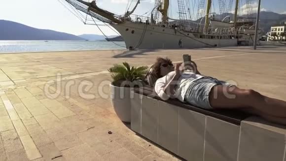女人躺在长廊的长凳上用手机浏览互联网视频的预览图