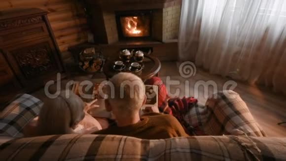 一对年长的夫妇认为一本家庭相册包裹在一条毯子上坐在舒适的壁炉旁视频的预览图