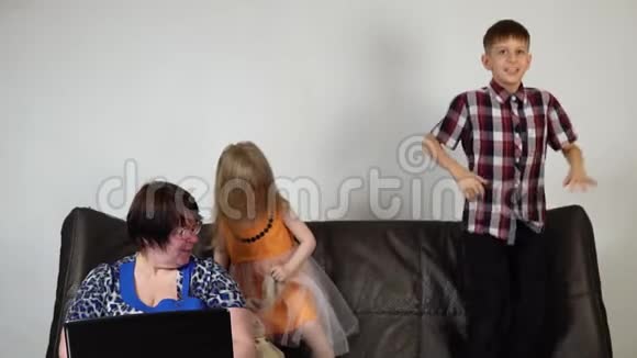 孩子们在沙发上跳跃一个沮丧的祖母正在使用笔记本电脑视频的预览图