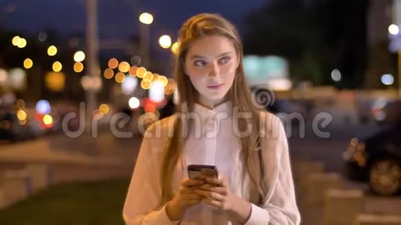 一个年轻迷人的女孩正在夏季傍晚在市中心的智能手机上输入信息视频的预览图