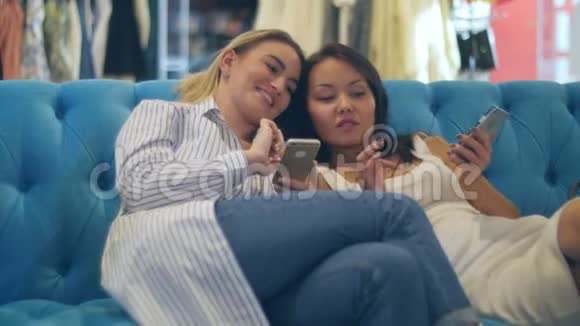 快乐的购物女性使用智能手机坐在购物中心大笑视频的预览图