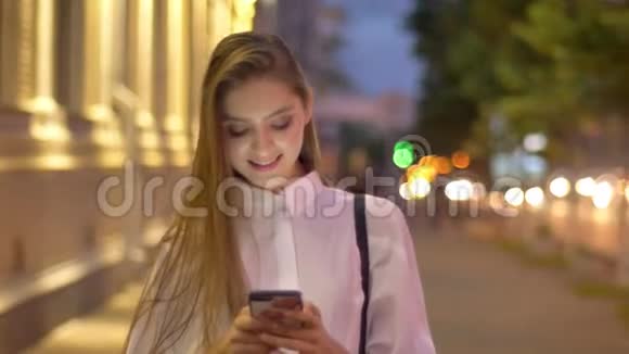 年轻迷人的有兴趣的女孩正在夏天的晚上在智能手机上输入信息微笑着交流视频的预览图