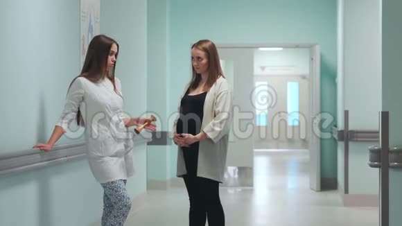 一位孕妇站在移植中心的走廊里和一位身穿白色长袍的医生交流视频的预览图