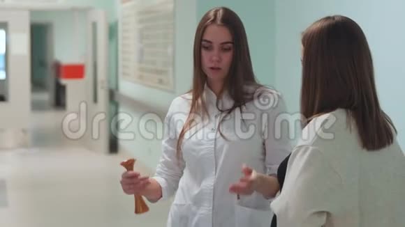 一位孕妇站在移植中心的走廊里和一位身穿白色长袍的医生交流视频的预览图