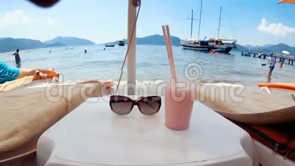 4k太阳镜和鸡尾酒的特写镜头桌上两根吸管放在海边的日光浴床之间视频的预览图