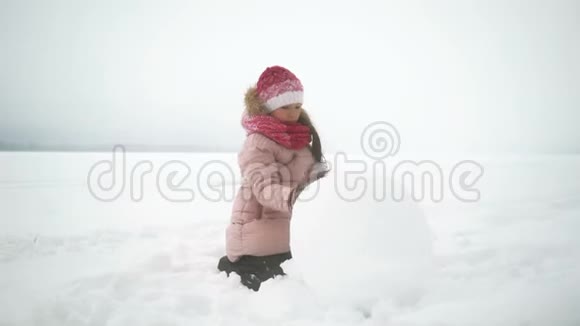 女孩在冬天为雪人滚动大雪球视频的预览图