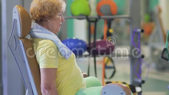 快乐的奶奶在健身房训练她的腿并在摄像机上显示拇指视频的预览图