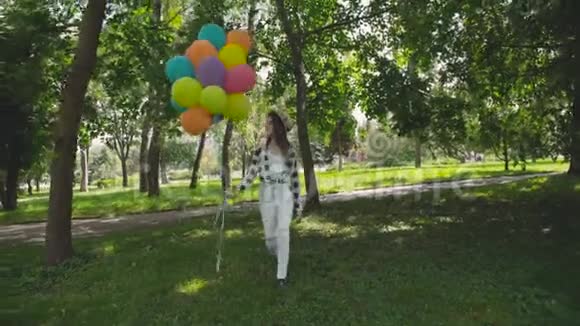快乐的小女孩走在绿色阳光的公园里手里拿着五颜六色的气球视频的预览图