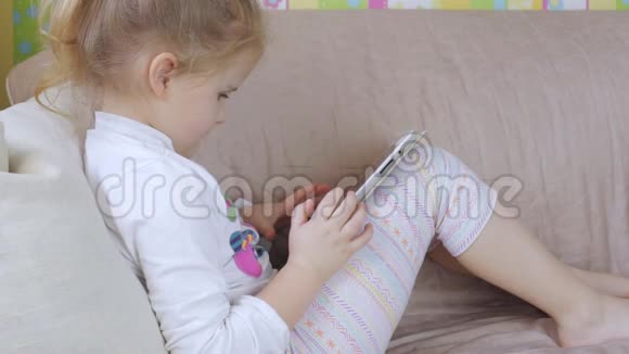 可爱的小女孩家里有平板电脑一个躺在沙发上用平板电脑的女孩视频的预览图