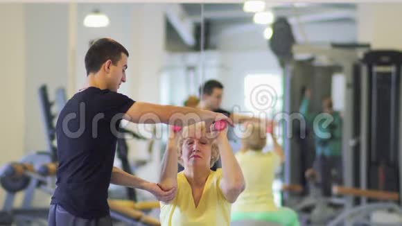 老年妇女在健身房用哑铃和教练一起做运动视频的预览图