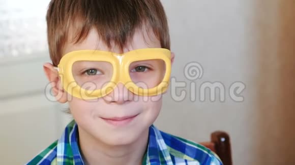 微笑的男孩穿着安全的黄色护目镜坐在桌子旁看着相机家庭化学实验视频的预览图