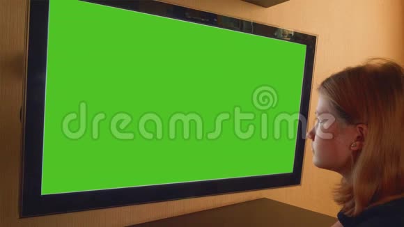 女孩坐在电视机前用绿色屏幕观看视频的预览图
