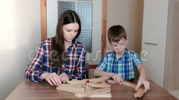 一起玩妈妈和儿子正在建造一条木铁路桌子旁坐着隧道视频的预览图