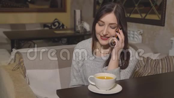 一个咖啡馆里的布鲁内特女士正在喝茶打电话视频的预览图