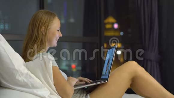 一位年轻女士正在用笔记本电脑交谈她坐在床上背着一个背景的摩天轮剪影视频的预览图