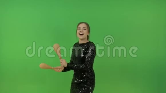 漂亮的白人女孩穿着黑色闪亮的连衣裙玩得开心和马拉卡斯跳舞在绿色的背景上视频的预览图