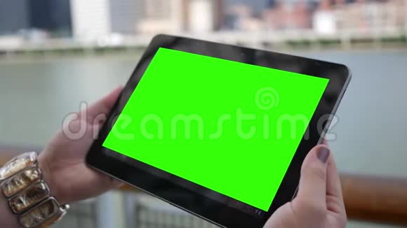 白天城市附近的时髦女性手持绿色屏幕平板电脑视频的预览图
