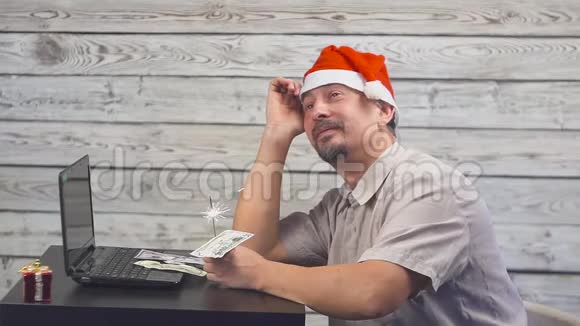 一个戴着圣诞帽手里拿着孟加拉火焰火和笔记本电脑的梦中人下降的货币美元视频的预览图
