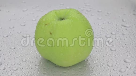一整个成熟的苹果在一滴露水中旋转躺在白色的潮湿背景上视频的预览图