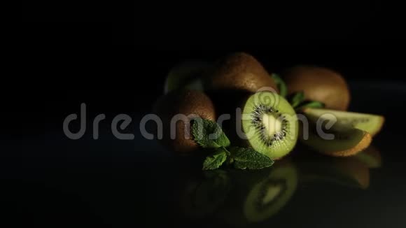 美味多汁的猕猴桃和薄荷在黑色的桌子上旋转着几维树在桌子上的倒影碎片视频的预览图