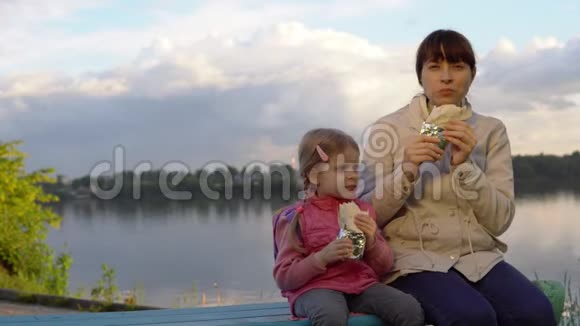 妈妈和女儿一起在池塘旁边的街道上吃甜甜圈视频的预览图