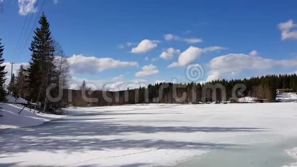 在一个美丽的阳光明媚的日子里挪威一个冰封的湖泊的全景与白雪环绕的树木中的房屋视频的预览图