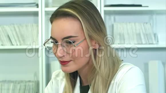戴眼镜的漂亮年轻女医生坐在办公桌前视频的预览图