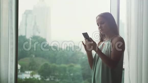 年轻漂亮的黑发女商人用手机站在全景窗口与城市景色4k3840x2160视频的预览图