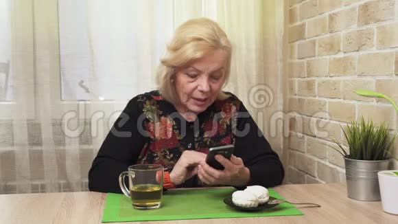 快乐的老妇人喝茶用智能手机视频的预览图