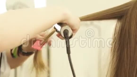 发型师用发钳和梳子在美容院做发型把理发师整理好长发视频的预览图