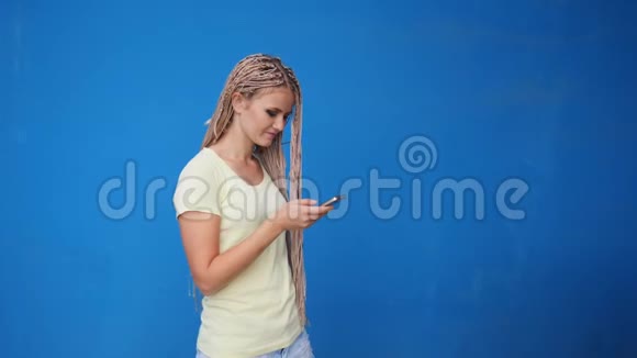 智能手机女人在电话里笑着蓝色背景美丽的年轻女性带辫子随意视频的预览图