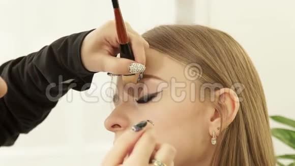 化妆师在美容学校用化妆刷化妆眼睛把脸贴紧为年轻人化妆视频的预览图