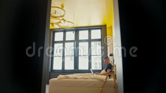 早晨年轻人躺在一张床上手提电脑躺在舒适的公寓里视频的预览图