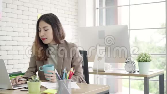 两位年轻的亚洲女商人在小企业的办公室里一起工作高兴地坐在那里阅读报告或文件视频的预览图