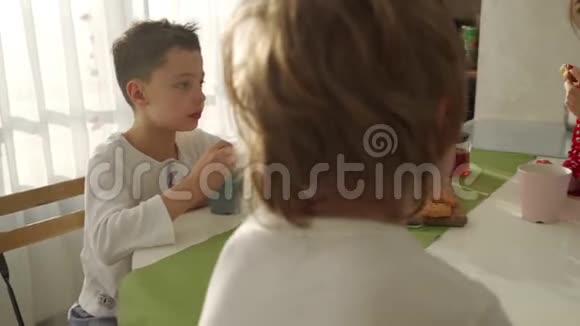 两个男孩在现代厨房吃早餐男孩吃带牛奶的饼干厨房里的白色桌子母亲和两个儿子视频的预览图