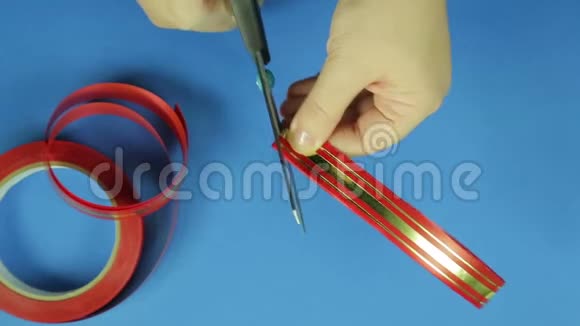 女性的手用剪刀剪角作为红色丝带礼物蝴蝶结蓝色背景视频的预览图