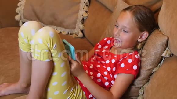 在舒适的客厅里快乐少女在沙发上用手机视频的预览图