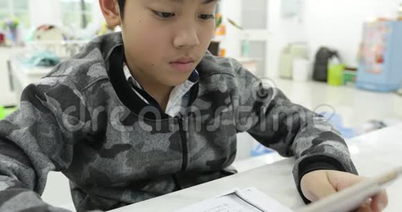 可爱的亚洲男孩使用平板电脑年轻的十几岁男孩在数字平板电脑上做家庭作业带着微笑的脸视频的预览图