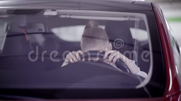扎着马尾辫的年轻女子坐在红色的车上头靠在方向盘上视频的预览图