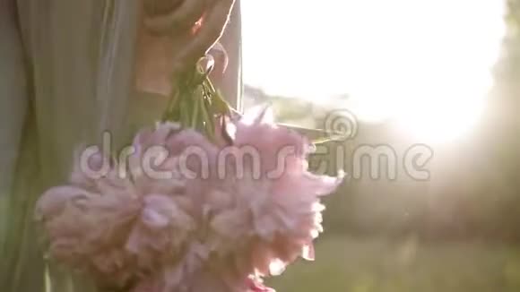 背面追踪一个穿着鲜艳衣服的女人走在绿色草地上的镜头她身上有一束粉红色的花视频的预览图