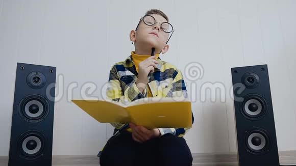 一个戴着教科书眼镜的金发小男孩坐在家里的地板上在里面记录了一些有趣的东西视频的预览图