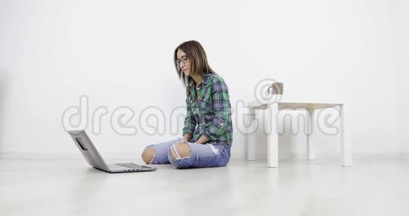 年轻漂亮的女孩坐在家里的地板上用笔记本电脑打视频电话视频的预览图