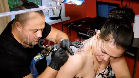在一家纹身沙龙里一位专家正在做一个女人背上纹身一个花饰一个人戴着特殊的手套工作视频的预览图