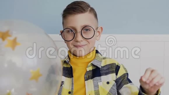 肖像一个戴着圆眼镜的英俊男孩拿着气球用针扎穿它气球里面是金色的视频的预览图