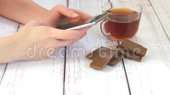 一个女孩的手拿着智能手机在咖啡馆特写桌子上有一杯茶巧克力生活中的技术视频的预览图