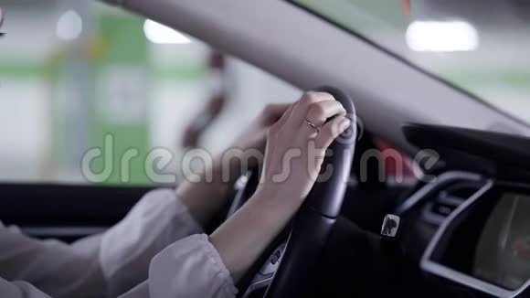 穿着白色衬衫的漂亮女孩坐在车里拿着方向盘在车库旁边视频的预览图